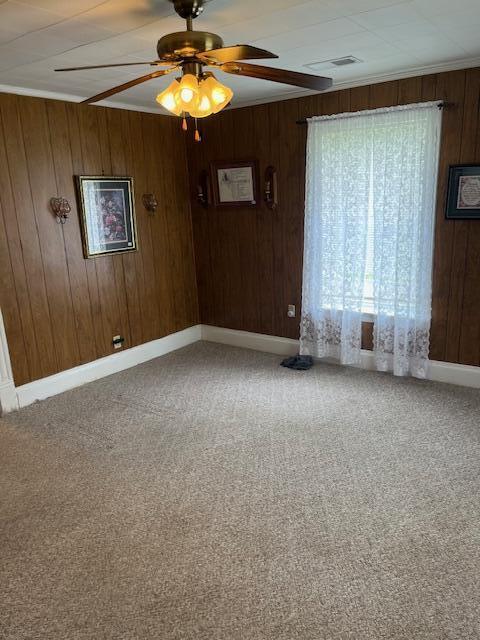 empty room with wooden walls, a ceiling fan, carpet floors, and baseboards