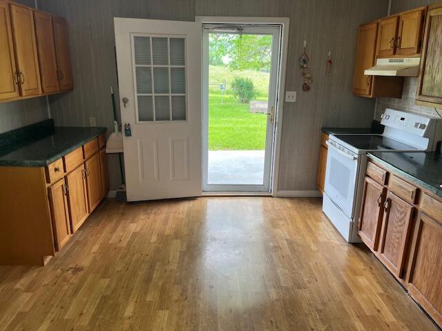 kitchen with white range with electric stovetop, under cabinet range hood, light wood finished floors, and dark countertops