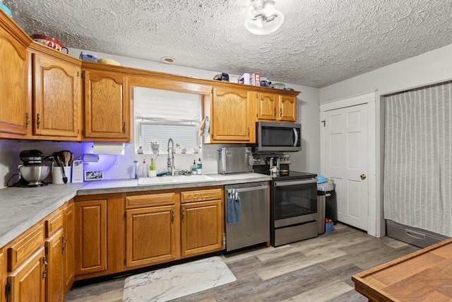 kitchen with appliances with stainless steel finishes, a sink, light countertops, light wood finished floors, and a textured ceiling