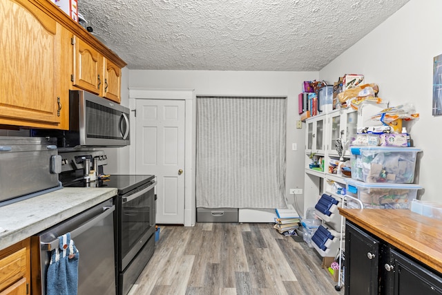 kitchen featuring stainless steel appliances, light wood-type flooring, light countertops, a textured ceiling, and brown cabinets