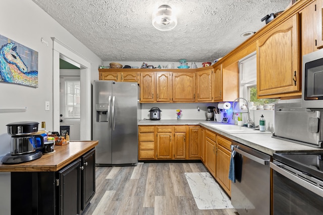 kitchen with appliances with stainless steel finishes, a sink, light wood-style floors, light countertops, and brown cabinetry