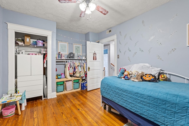 bedroom with a textured ceiling, wood finished floors, ceiling fan, and a closet