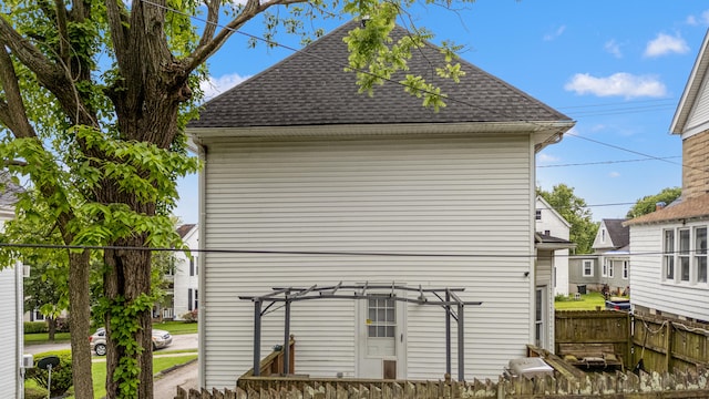 view of property exterior with roof with shingles, a pergola, and fence