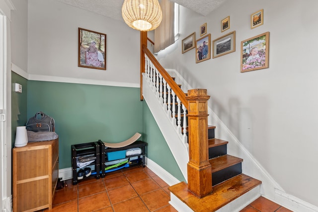 stairway featuring tile patterned flooring, baseboards, a chandelier, and a textured ceiling