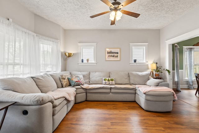 living area with a ceiling fan, healthy amount of natural light, wood finished floors, and a textured ceiling