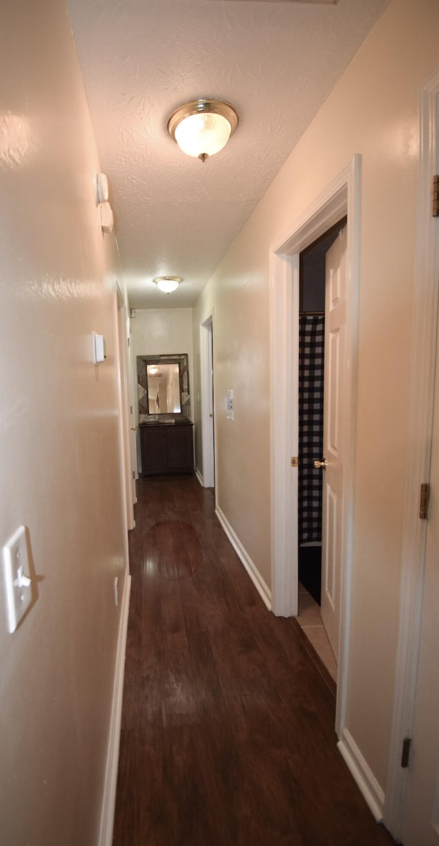corridor featuring wood finished floors, baseboards, and a textured ceiling
