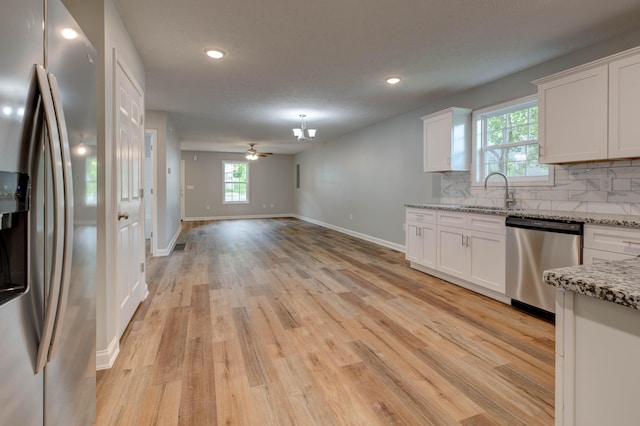kitchen with stainless steel appliances, a sink, light wood-style floors, decorative backsplash, and white cabinets
