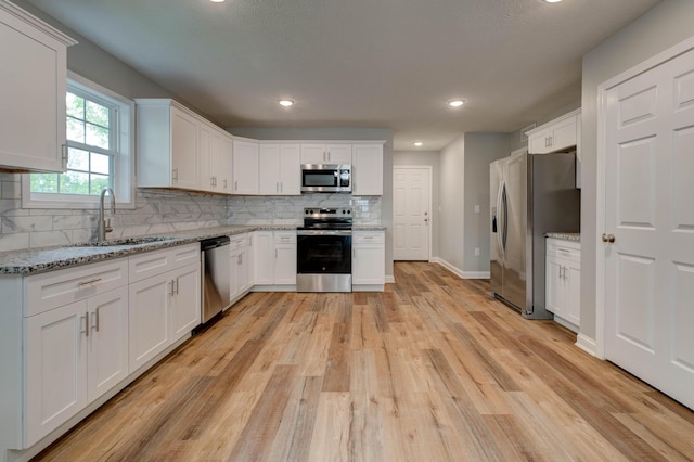 kitchen with appliances with stainless steel finishes, a sink, tasteful backsplash, light wood finished floors, and white cabinets
