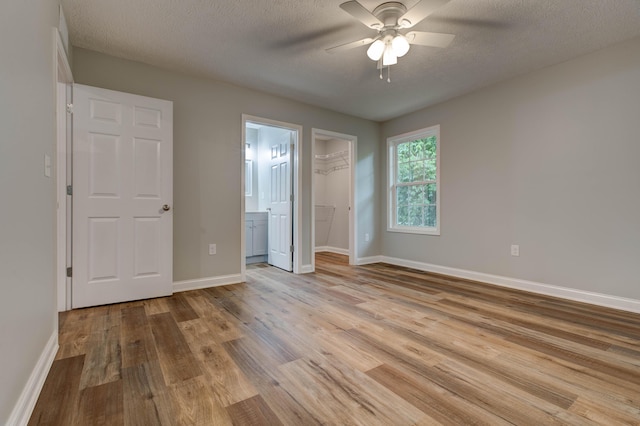 unfurnished bedroom with wood finished floors, baseboards, a walk in closet, a ceiling fan, and a textured ceiling