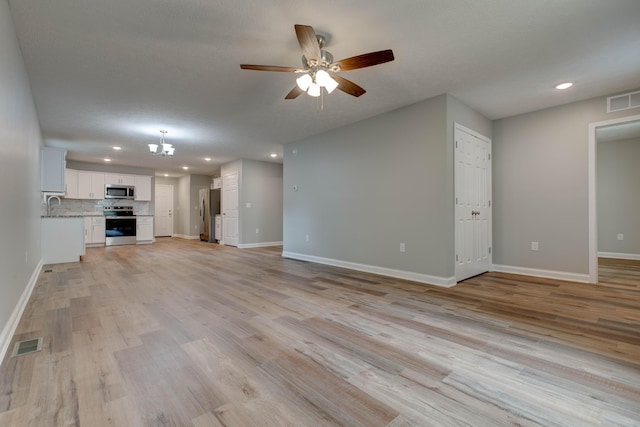 unfurnished living room with a ceiling fan, recessed lighting, baseboards, light wood-type flooring, and a chandelier