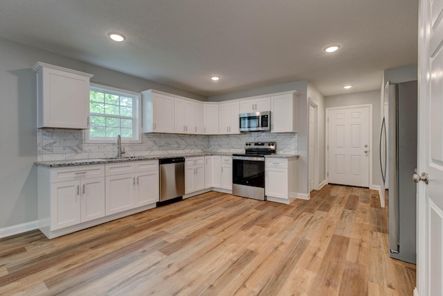 kitchen with stainless steel appliances, a sink, white cabinetry, decorative backsplash, and recessed lighting