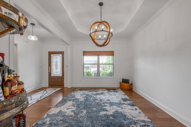 entrance foyer featuring dark wood-type flooring, a chandelier, a raised ceiling, crown molding, and baseboards