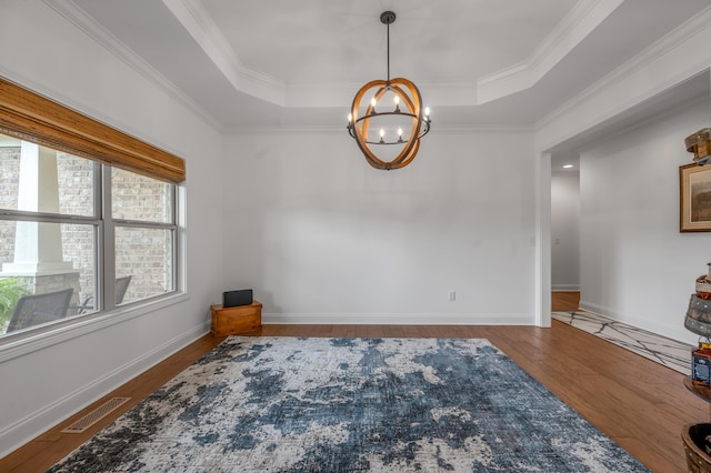 empty room with a chandelier, wood finished floors, a raised ceiling, ornamental molding, and baseboards