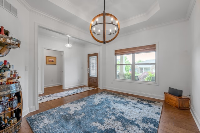 entrance foyer with hardwood / wood-style floors, a chandelier, ornamental molding, a raised ceiling, and baseboards