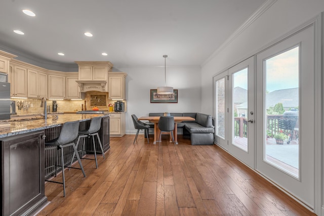kitchen with cream cabinetry, ornamental molding, decorative backsplash, a kitchen bar, and light stone countertops