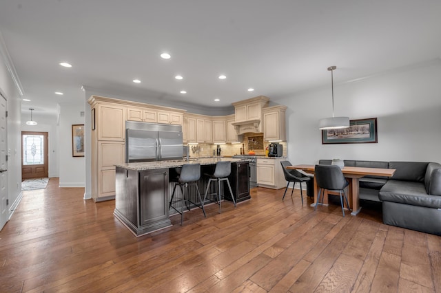 kitchen with premium appliances, ornamental molding, wood-type flooring, tasteful backsplash, and a center island with sink