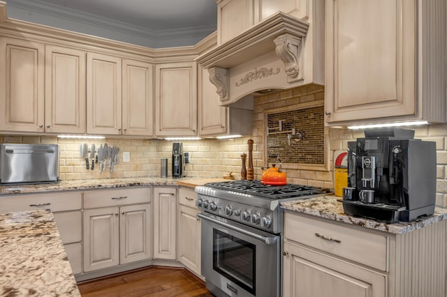 kitchen with stainless steel stove, custom exhaust hood, decorative backsplash, light wood-type flooring, and cream cabinets