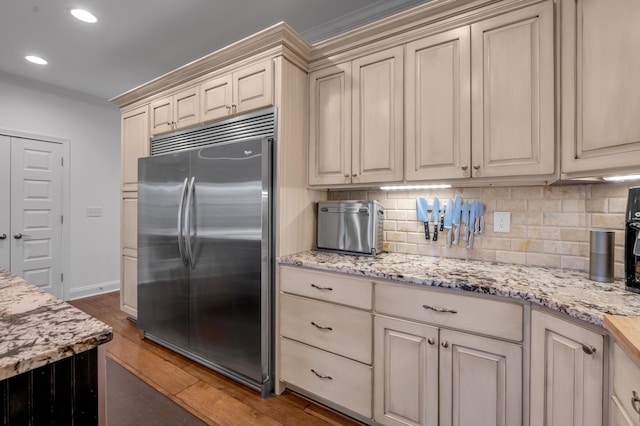 kitchen with stainless steel built in refrigerator, cream cabinets, wood finished floors, backsplash, and recessed lighting