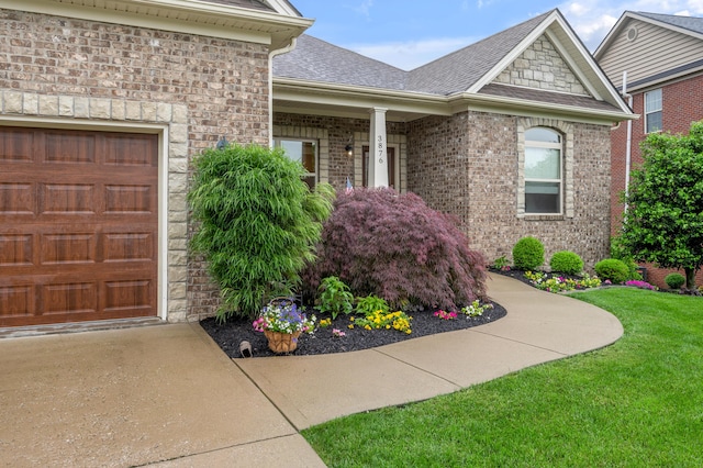 entrance to property with roof with shingles, a yard, an attached garage, stone siding, and driveway