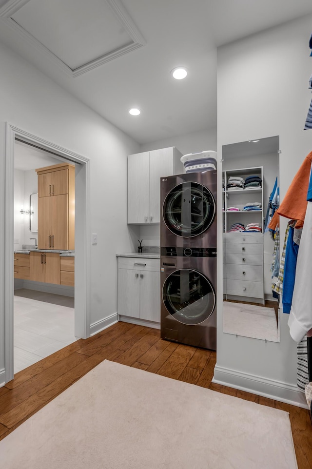 clothes washing area with stacked washing machine and dryer, cabinet space, light wood-style flooring, recessed lighting, and baseboards