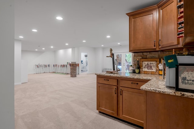 kitchen featuring light colored carpet, light stone counters, recessed lighting, brown cabinetry, and baseboards