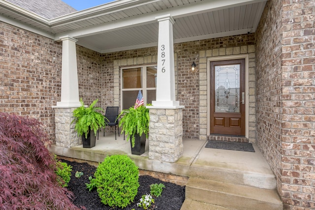 view of exterior entry with a porch and brick siding