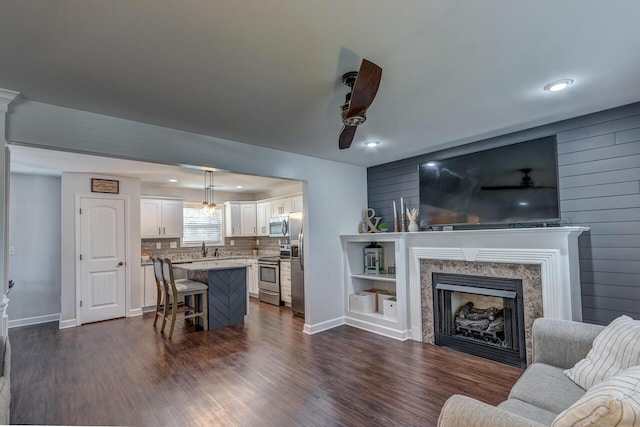 living room featuring dark wood-style floors, a premium fireplace, ceiling fan, recessed lighting, and baseboards