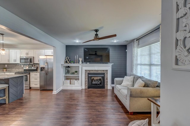 living area with a ceiling fan, dark wood-style floors, a fireplace, and baseboards