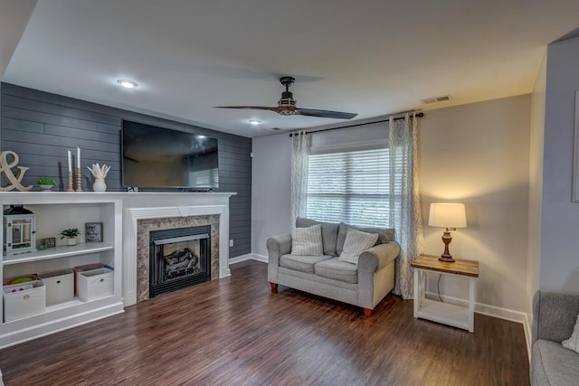 living area with baseboards, wood finished floors, a ceiling fan, a fireplace, and wooden walls