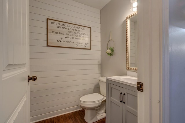 bathroom featuring wooden walls, toilet, vanity, and wood finished floors