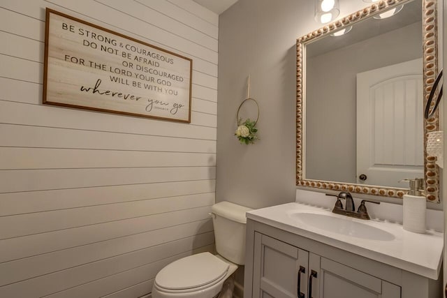bathroom featuring toilet, vanity, and wood walls