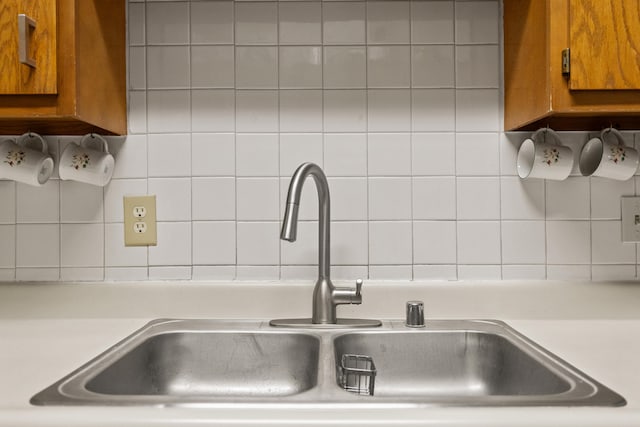 kitchen view of a sink, light countertops, brown cabinetry, and backsplash
