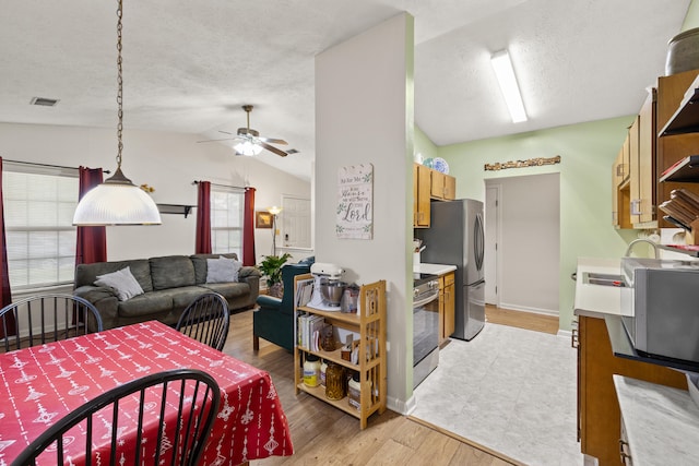 dining space with ceiling fan, vaulted ceiling, a textured ceiling, and light wood-style flooring