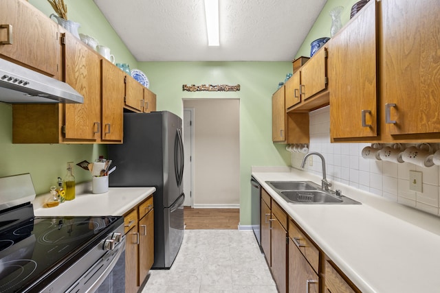 kitchen featuring appliances with stainless steel finishes, a sink, light countertops, brown cabinetry, and a textured ceiling