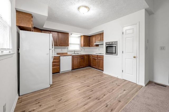 kitchen featuring white appliances, under cabinet range hood, a textured ceiling, light wood-type flooring, and light countertops