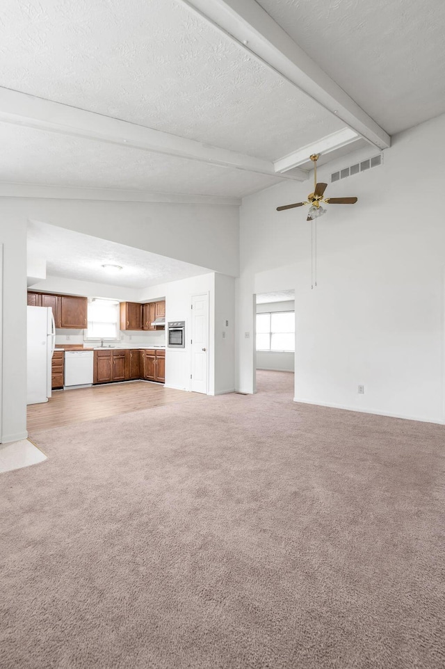 unfurnished living room with light carpet, plenty of natural light, beam ceiling, ceiling fan, and a textured ceiling