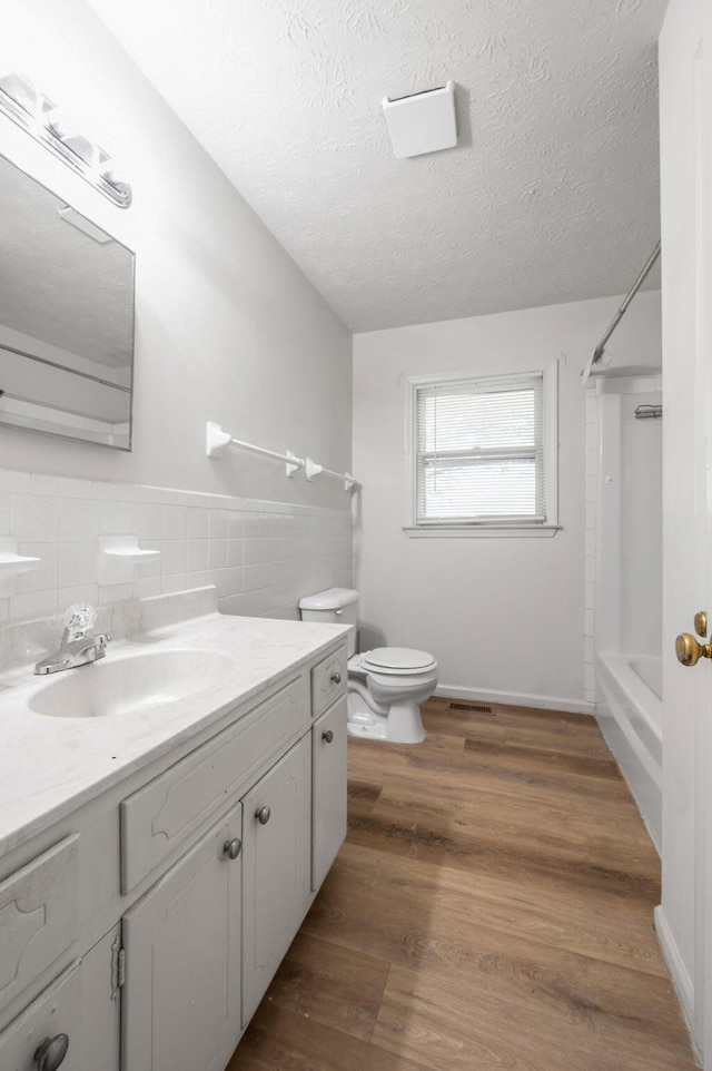 bathroom featuring toilet, vanity, a textured ceiling, bathtub / shower combination, and decorative backsplash