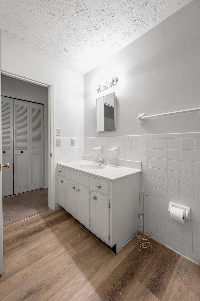 bathroom with tile walls, wood finished floors, a textured ceiling, vanity, and a wainscoted wall