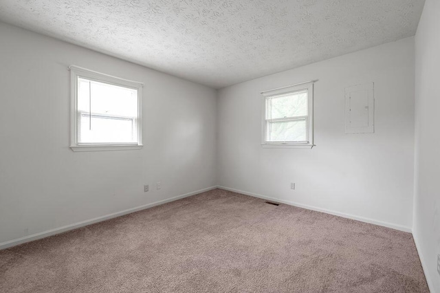 empty room with carpet flooring, a textured ceiling, baseboards, and electric panel