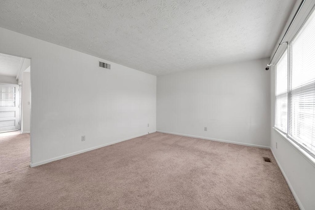 unfurnished room with light colored carpet, a textured ceiling, and baseboards