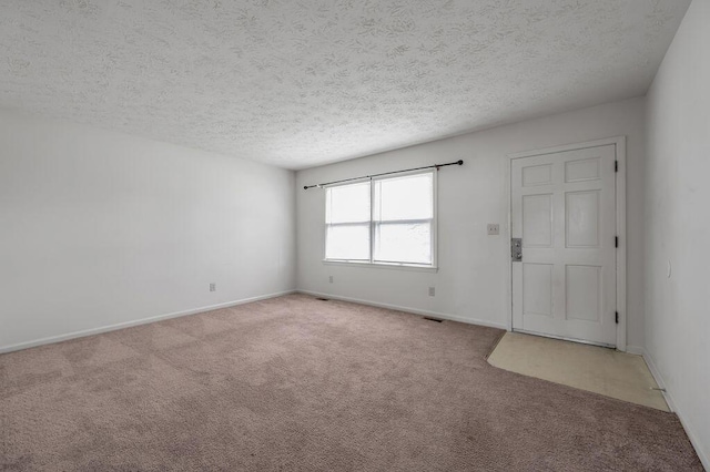 empty room with light colored carpet, a textured ceiling, and baseboards