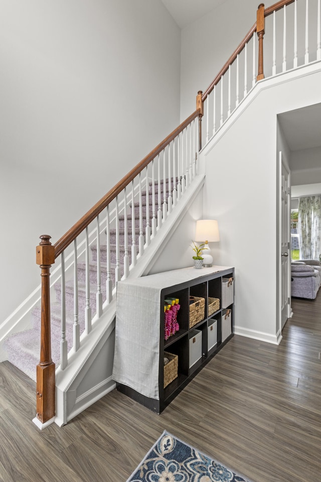 staircase with wood finished floors, baseboards, and a towering ceiling