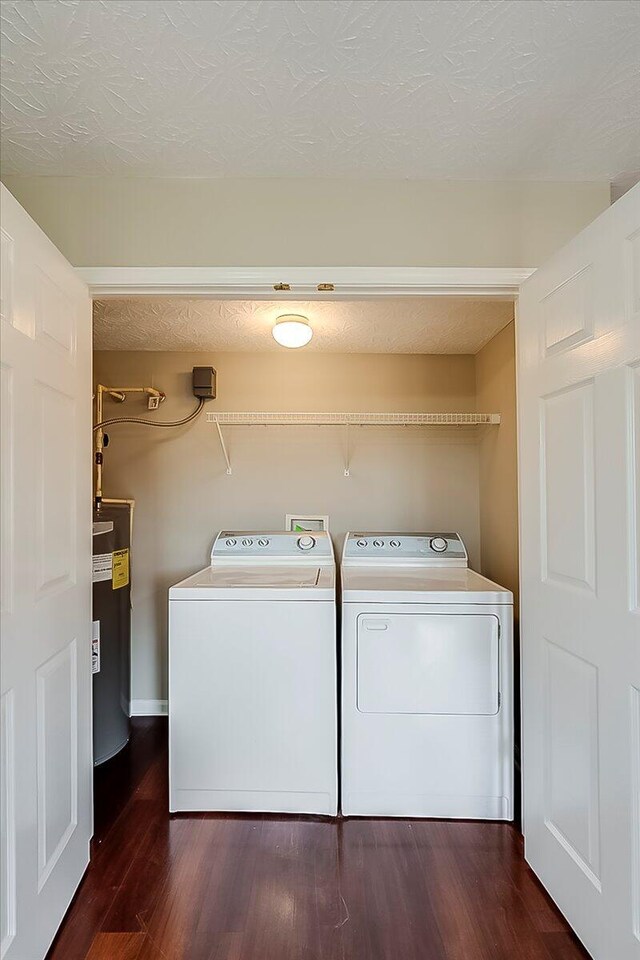 laundry room featuring washing machine and dryer, water heater, dark wood-style floors, and a textured ceiling