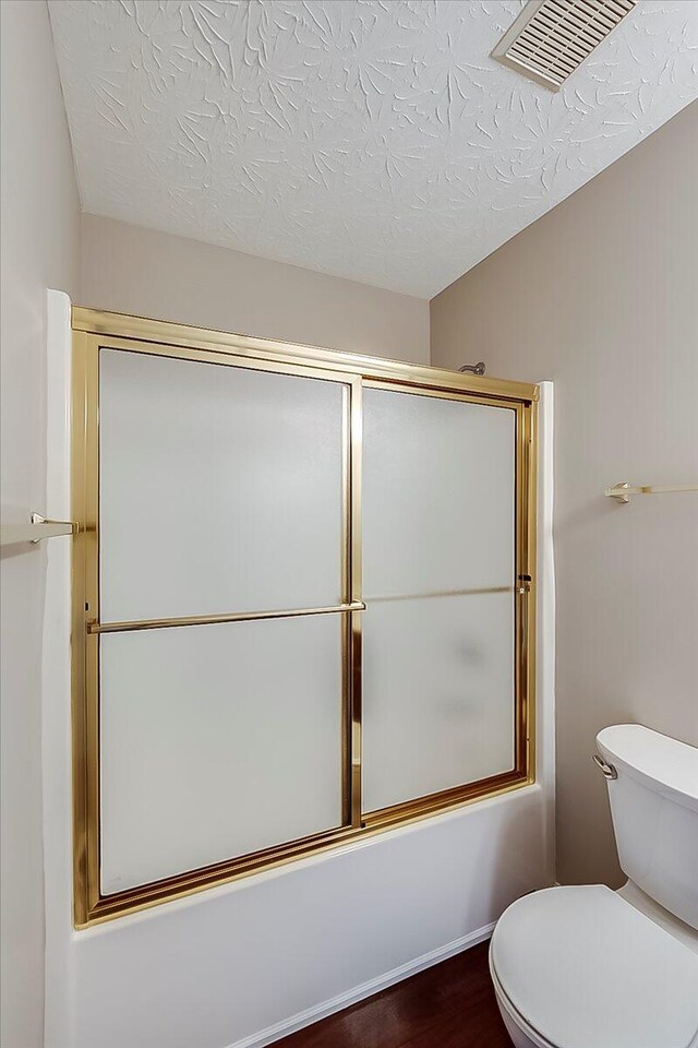 bathroom featuring shower / bath combination with glass door, toilet, a textured ceiling, and wood finished floors