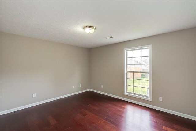spare room featuring dark wood finished floors, plenty of natural light, and baseboards