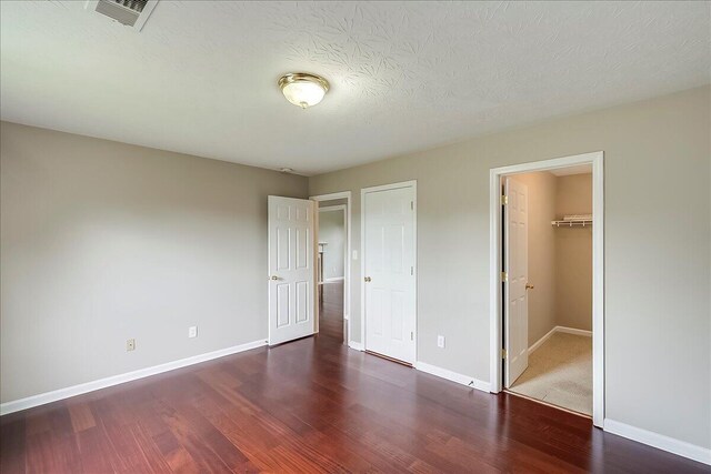 unfurnished bedroom with wood finished floors, baseboards, and a walk in closet