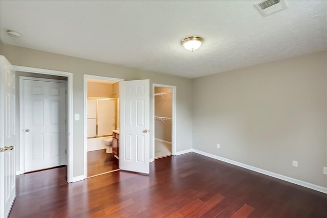 unfurnished bedroom with wood finished floors, baseboards, a walk in closet, and a closet