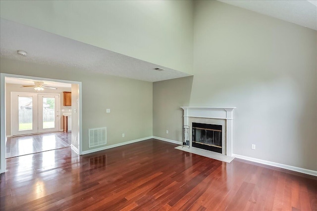 unfurnished living room featuring wood finished floors, a fireplace with flush hearth, baseboards, ceiling fan, and a towering ceiling