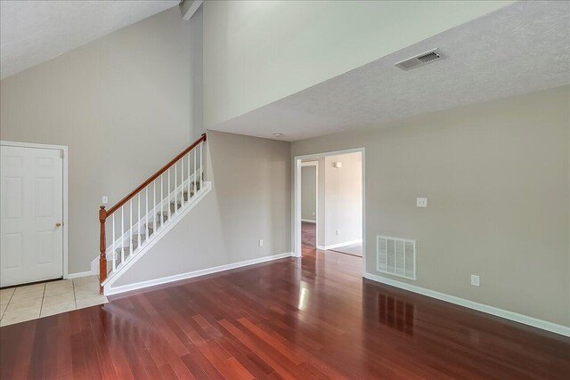spare room with wood finished floors, stairway, high vaulted ceiling, and baseboards