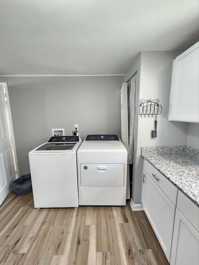 clothes washing area featuring independent washer and dryer, light wood-style flooring, and cabinet space